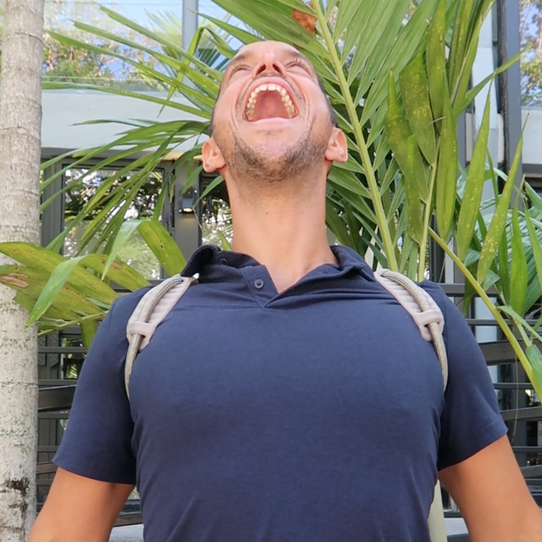 A content individual in an office setting, visibly pleased and relaxed while wearing The Back Transformer shoulder support brace.