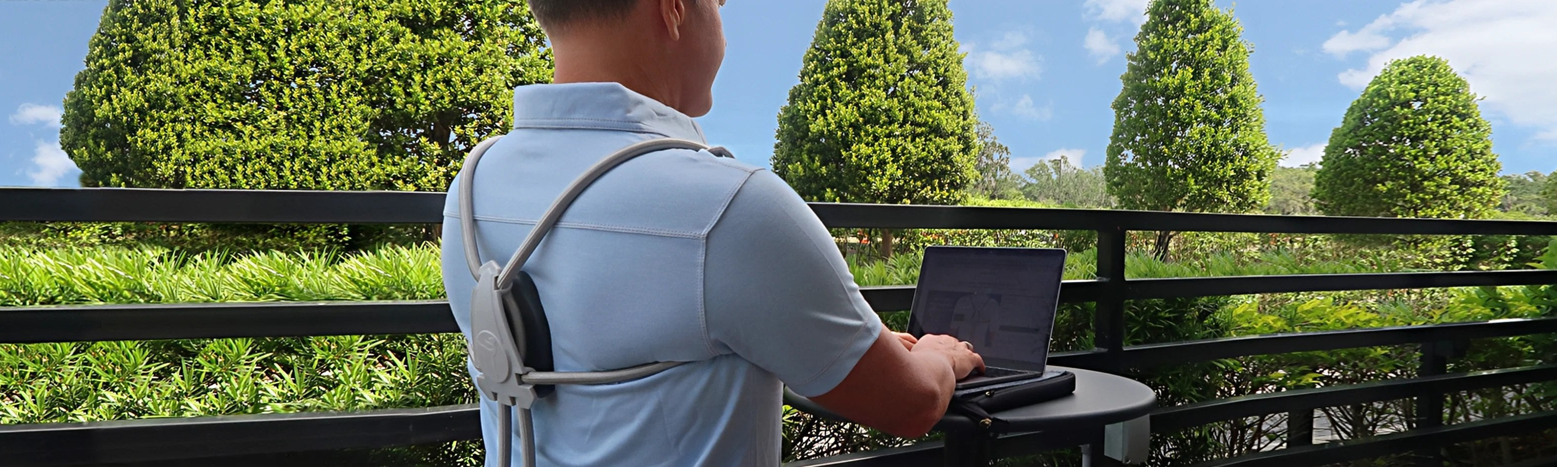 Someone wearing The Back Transformer posture corrector while working in front of a computer in an outdoor setting